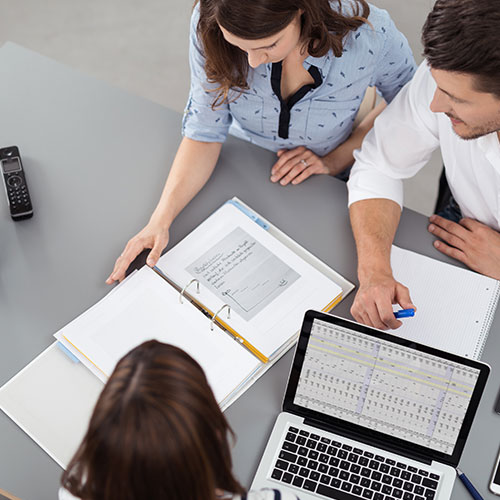 three people working with a laptop and binder