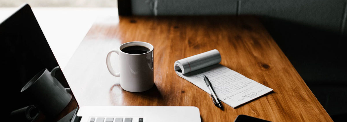 laptop and a notepad on a table with a phone and coffee cup