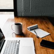 laptop and a notepad on a table with a phone and coffee cup