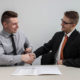 two men shaking hands over a file of legal papers